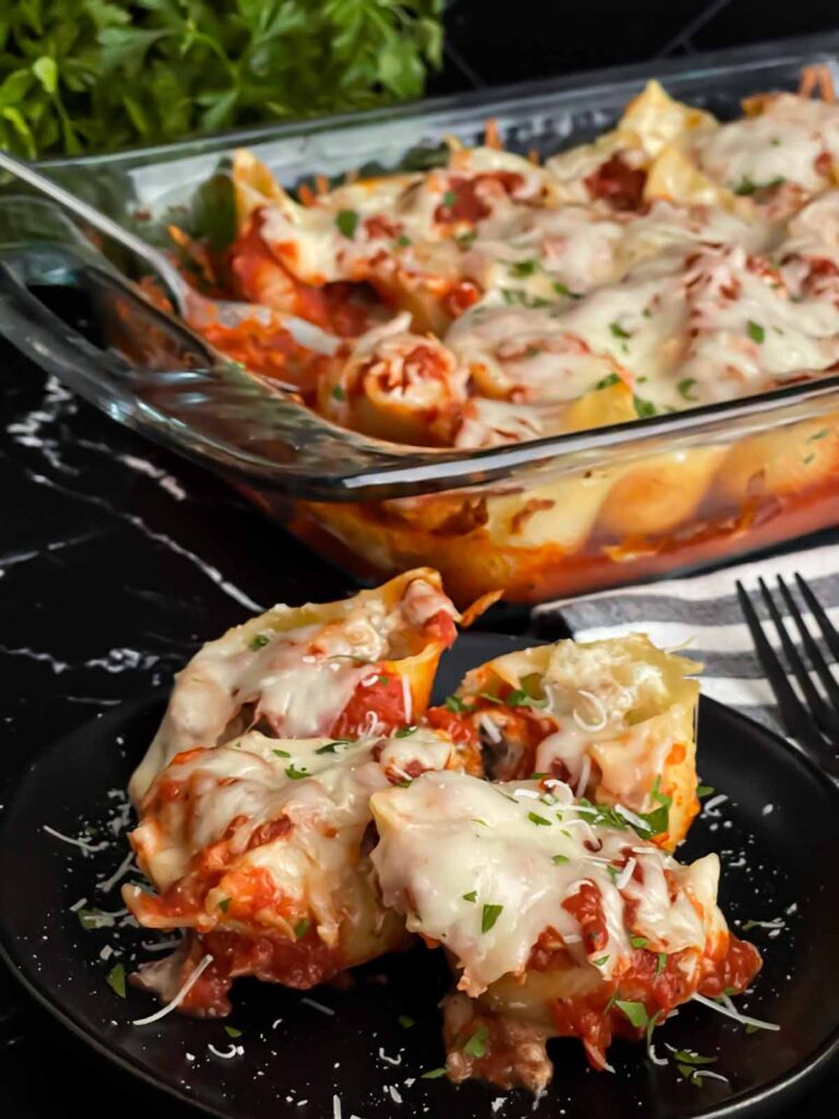 Italian sausage stuffed shells on a black plate with a casserole of it in the background.