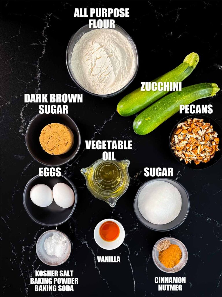 Zucchini bread recipe ingredients on a dark surface.