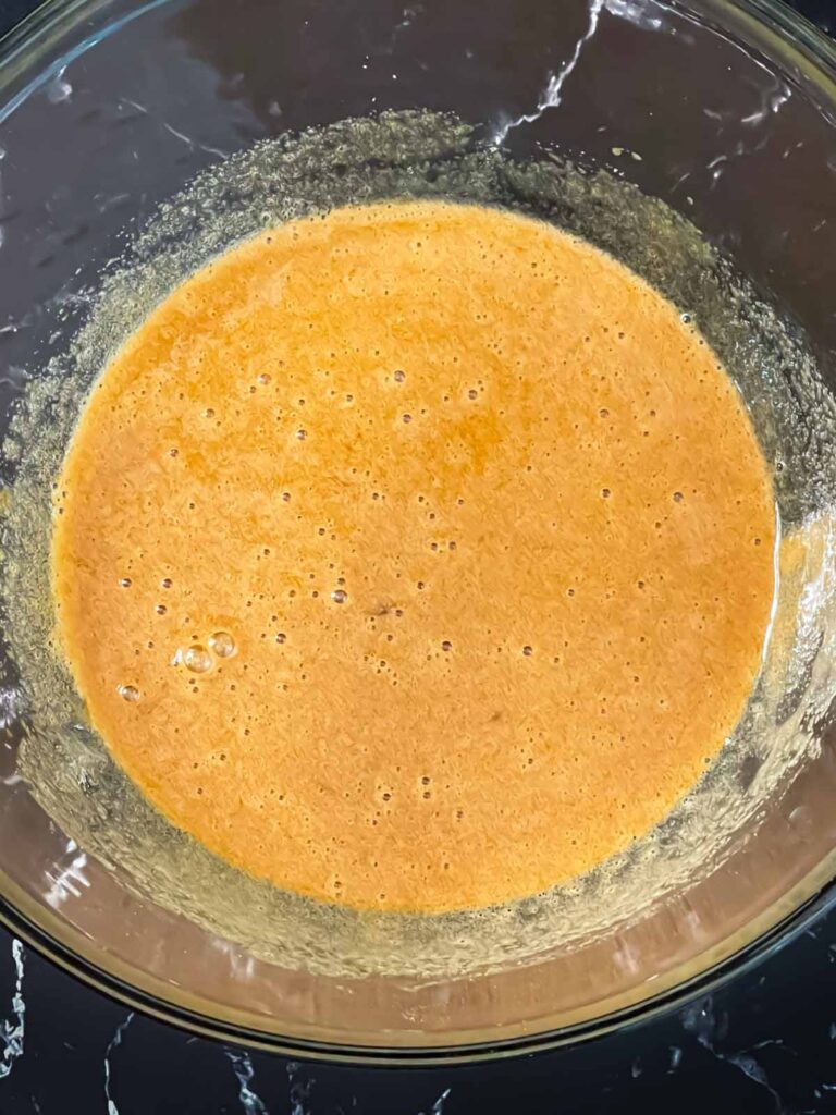 Eggs and sugars whisked in a glass bowl for zucchini bread recipe.