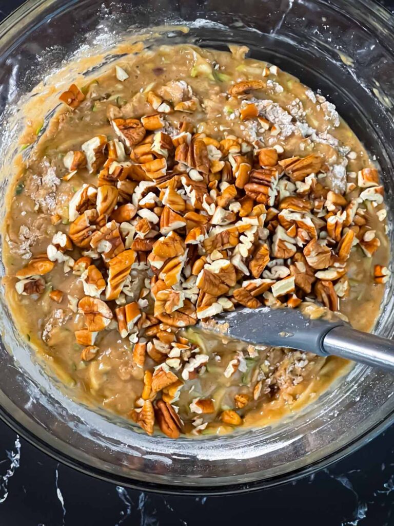 Chopped pecans added to the zucchini bread batter in a glass bowl.