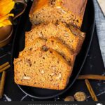 Sliced zucchini bread loaf on a dark oval platter on a dark surface.