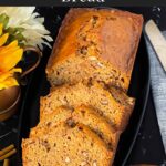 Sliced zucchini bread loaf on a dark oval platter on a dark surface.