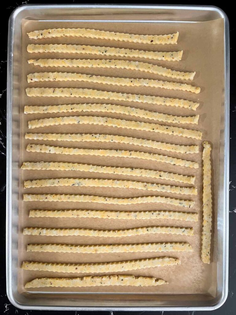 Cheddar cheese and herb straws on a baking sheet ready to be baked.