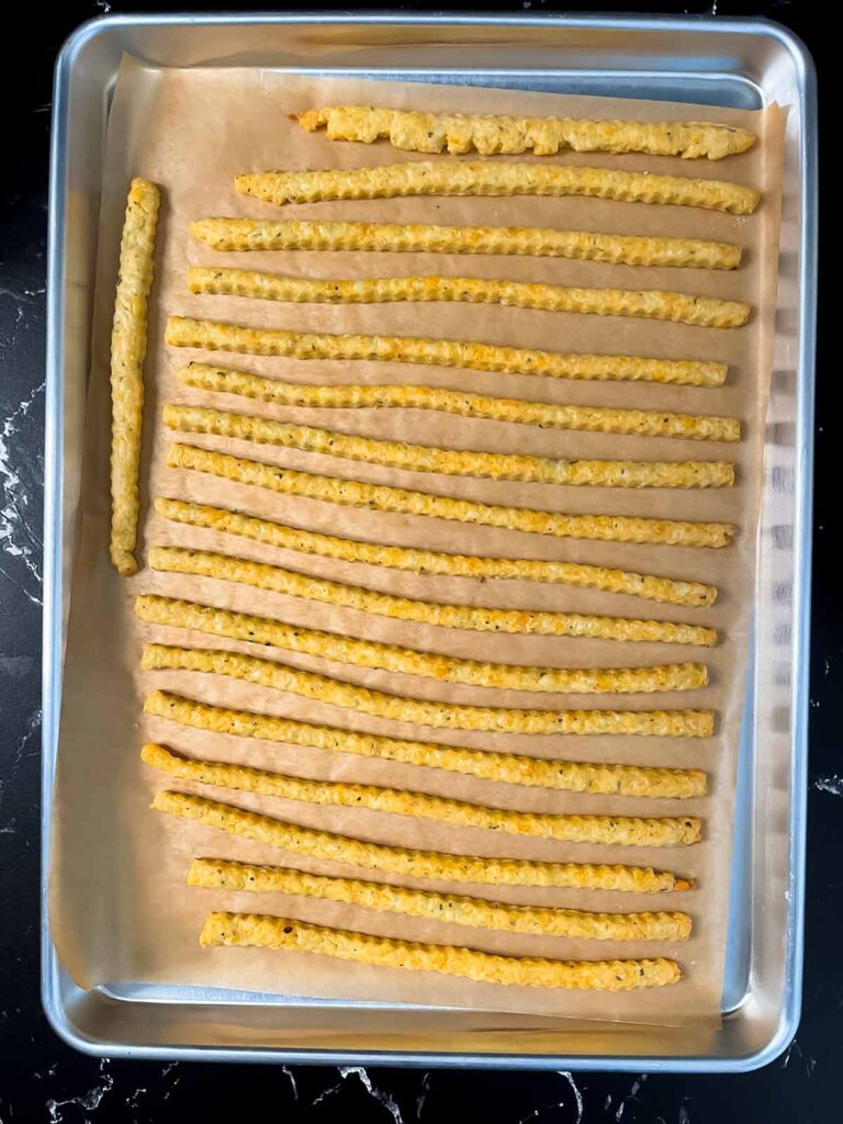 Baked cheddar cheese and herb straws on a baking sheet.