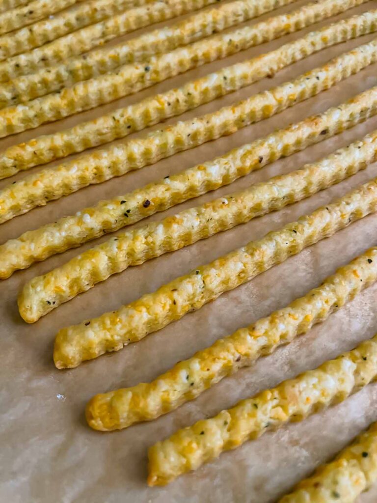 Baked cheddar cheese and herb straws on a baking sheet.