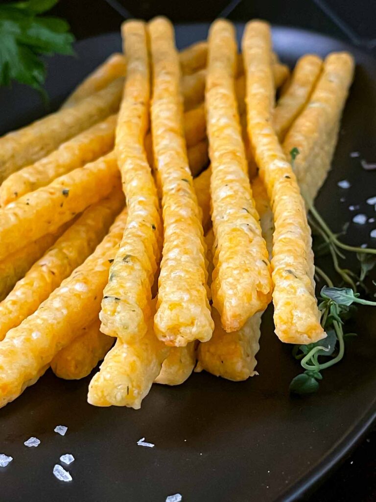 Cheddar and herb cheese straws on a black plate.