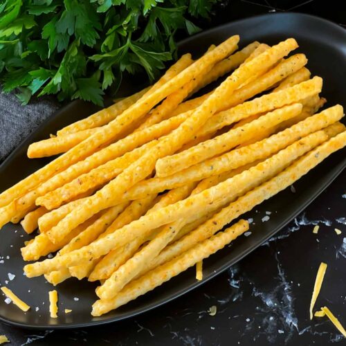 Cheddar and herb cheese straws on a black plate.