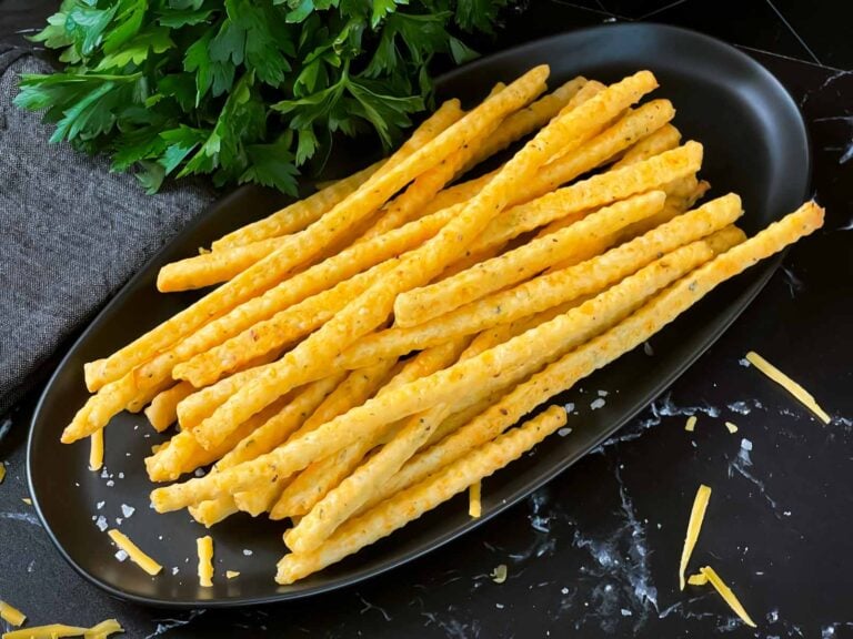 Cheddar and herb cheese straws on a black plate.