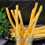 Cheddar and herb cheese straws on a black plate.