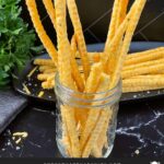 Cheddar and herb cheese straws on a black plate.