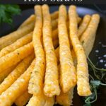 Cheddar and herb cheese straws on a black plate.