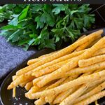 Cheddar and herb cheese straws on a black plate.