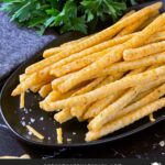 Cheddar and herb cheese straws on a black plate.