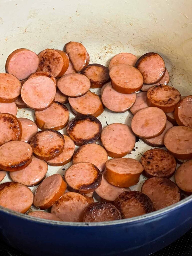 Smoked sausage being browned in a dutch oven.