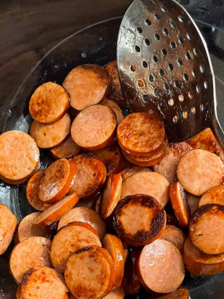 Removing browned smoked sausage from a dutch oven.