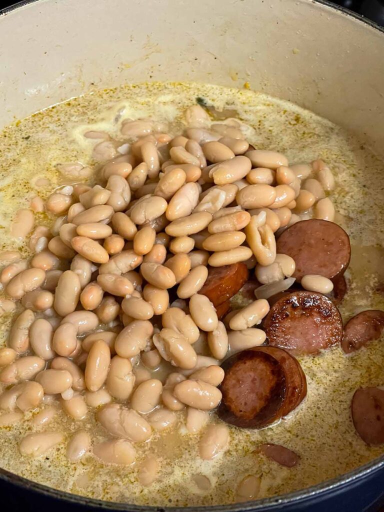 Adding beans and browned smoked sausage to the soup.