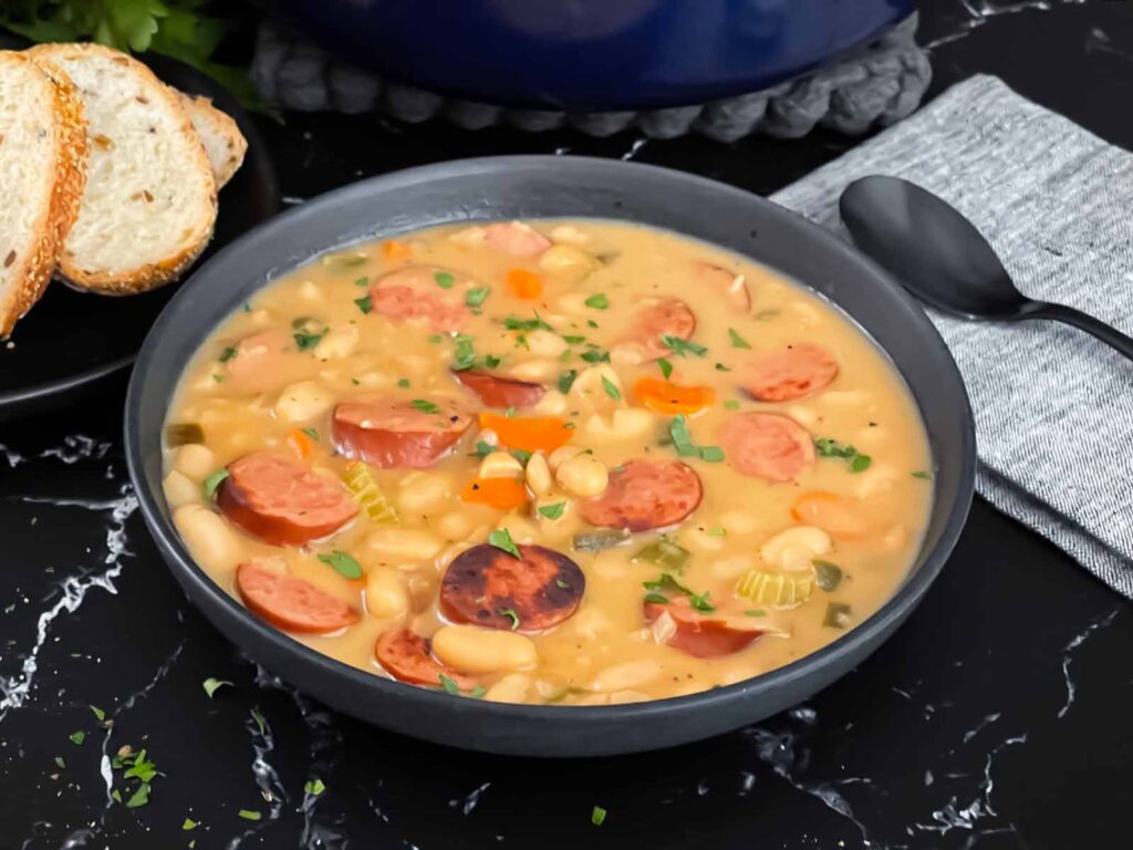 Bean soups with smoked sausage with bread and parsley in the background.