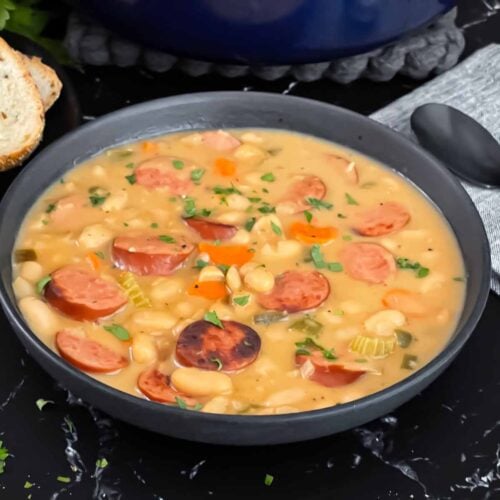 Bean soups with smoked sausage with bread and parsley in the background.