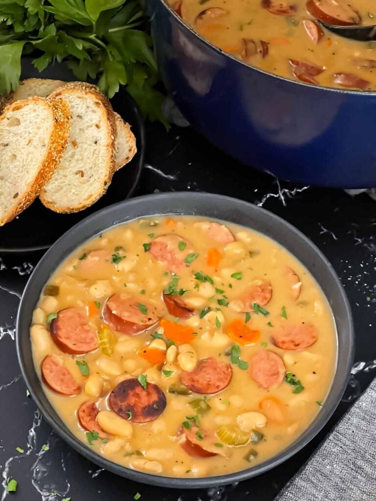 Bean soups with smoked sausage with bread and parsley in the background.