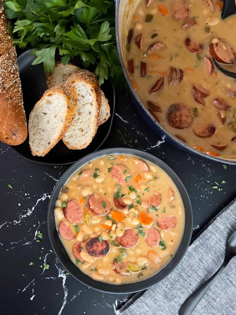 Bean soups with smoked sausage with bread and parsley in the background.