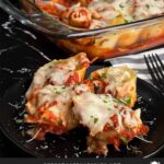 Italian sausage stuffed shells in a casserole dish with a serving on a black plate.