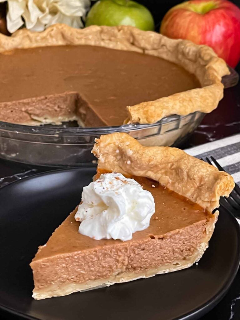 Apple butter pie with a sliced on a dark plate, garnished with whipped cream.