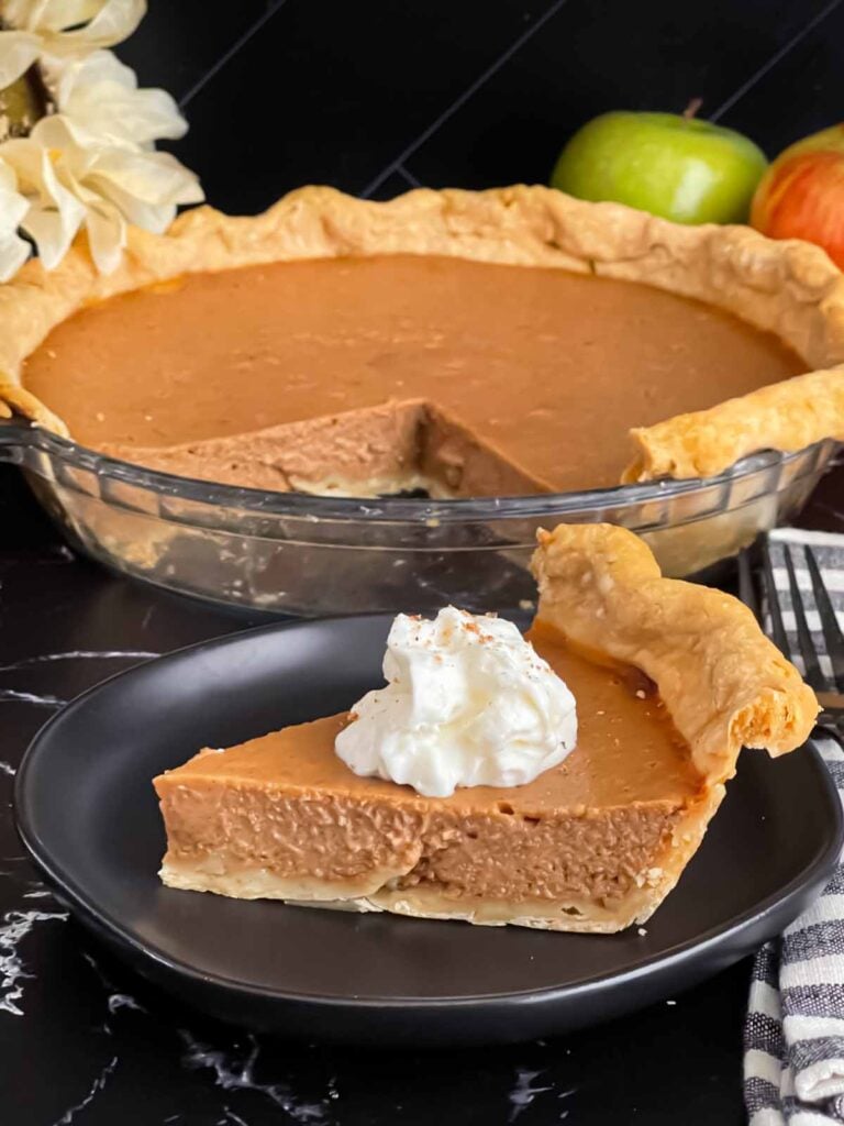 Apple butter pie with a sliced on a dark plate, garnished with whipped cream.