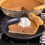 Apple butter pie with a sliced on a dark plate, garnished with whipped cream.