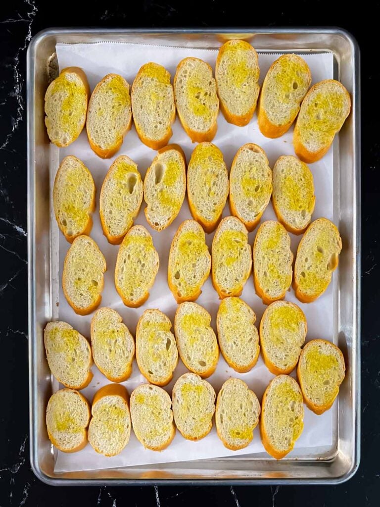 Baguette slices with olive oil on a baking sheet.