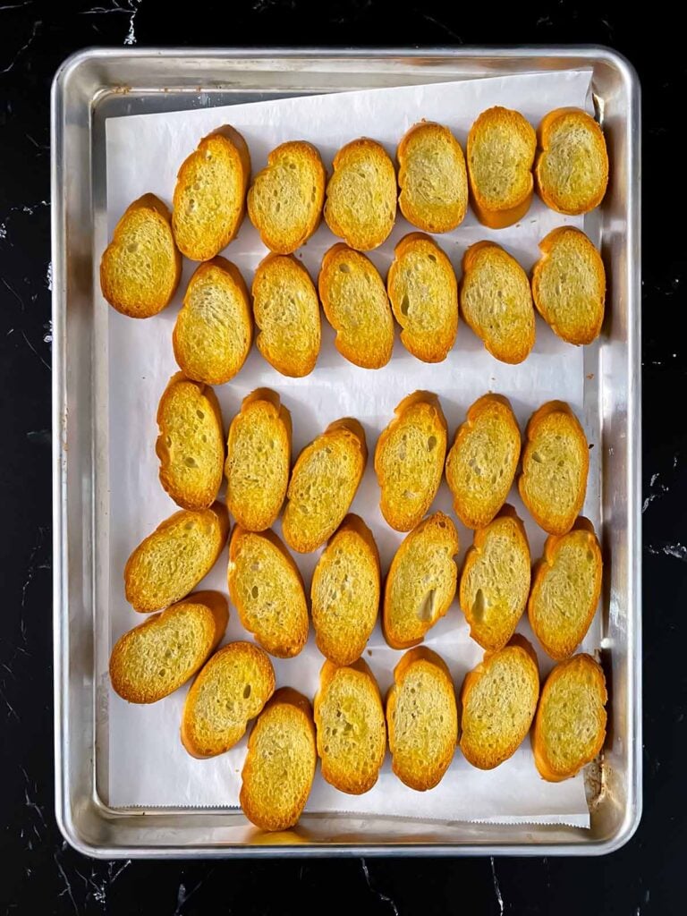 Toasted baguette slices with olive oil on a baking sheet.