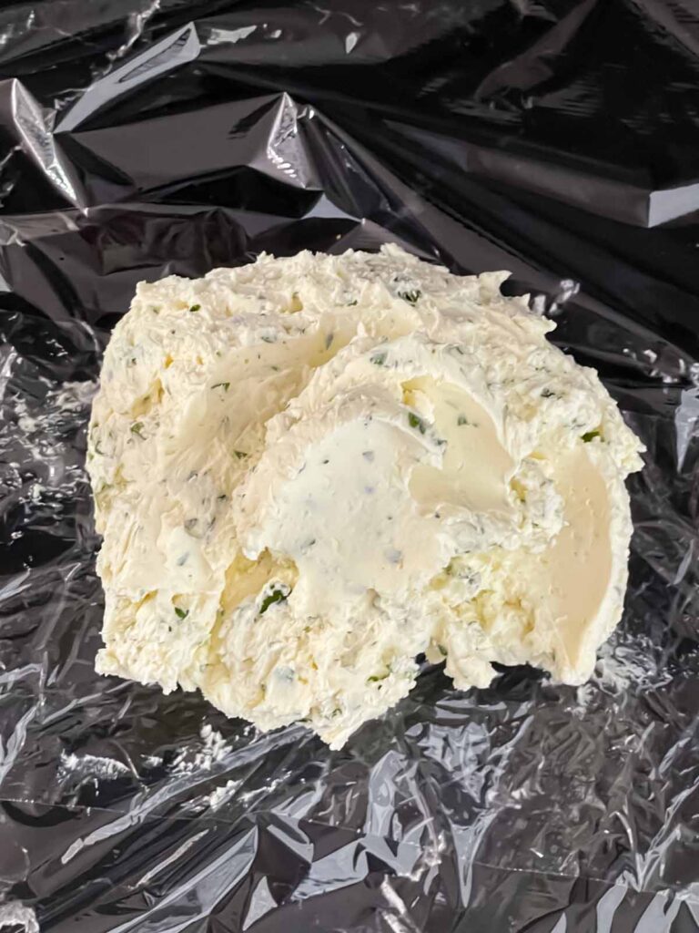 A garlic herb cheese ball mixture ready to be formed into a ball on plastic wrap.