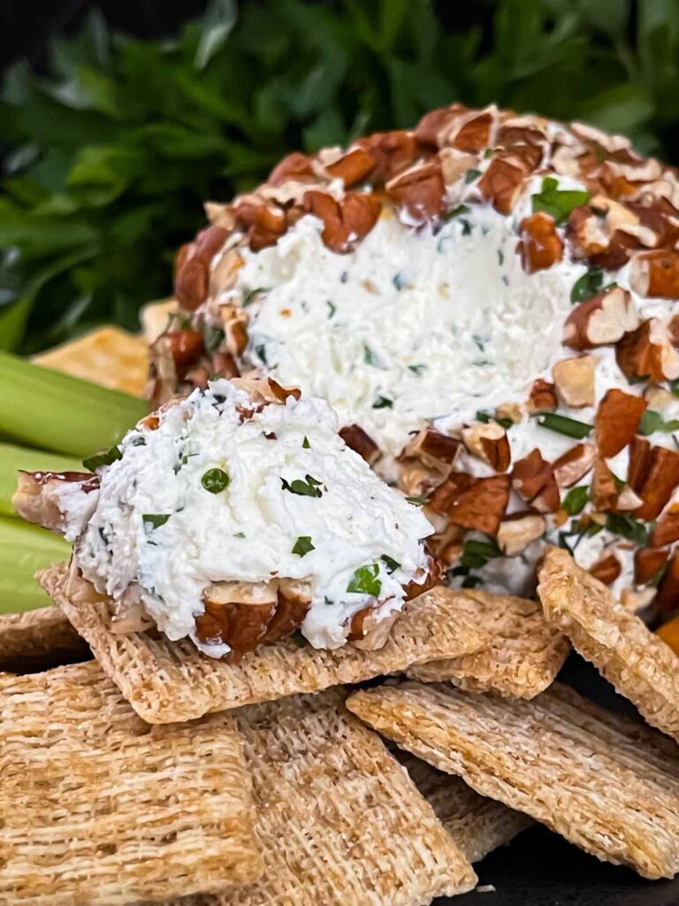 A garlic herb cheese ball on a black plate with crackers and vegetables.