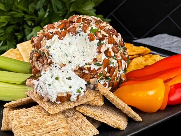 A garlic herb cheese ball on a black plate with crackers and vegetables.