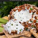 A garlic herb cheese ball on a black plate with crackers and vegetables.