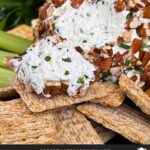 A garlic herb cheese ball on a black plate with crackers and vegetables.