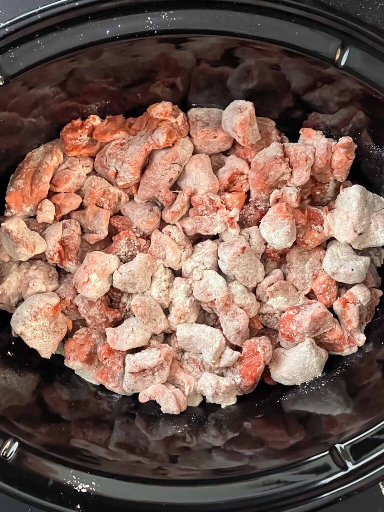 Flour-dusted stew meat in a slow cooker.