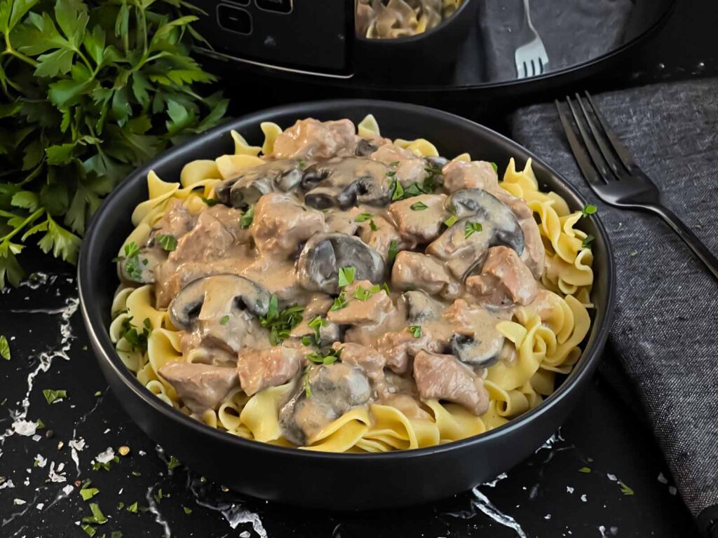 Slow cooker beef stroganoff in a dark bowl, garnished with chopped parsley.