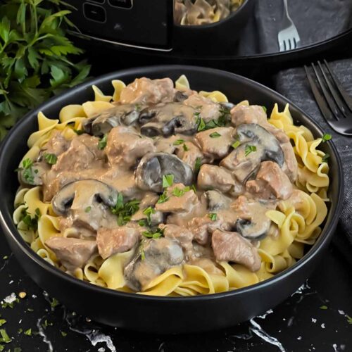 Slow cooker beef stroganoff in a dark bowl, garnished with chopped parsley.