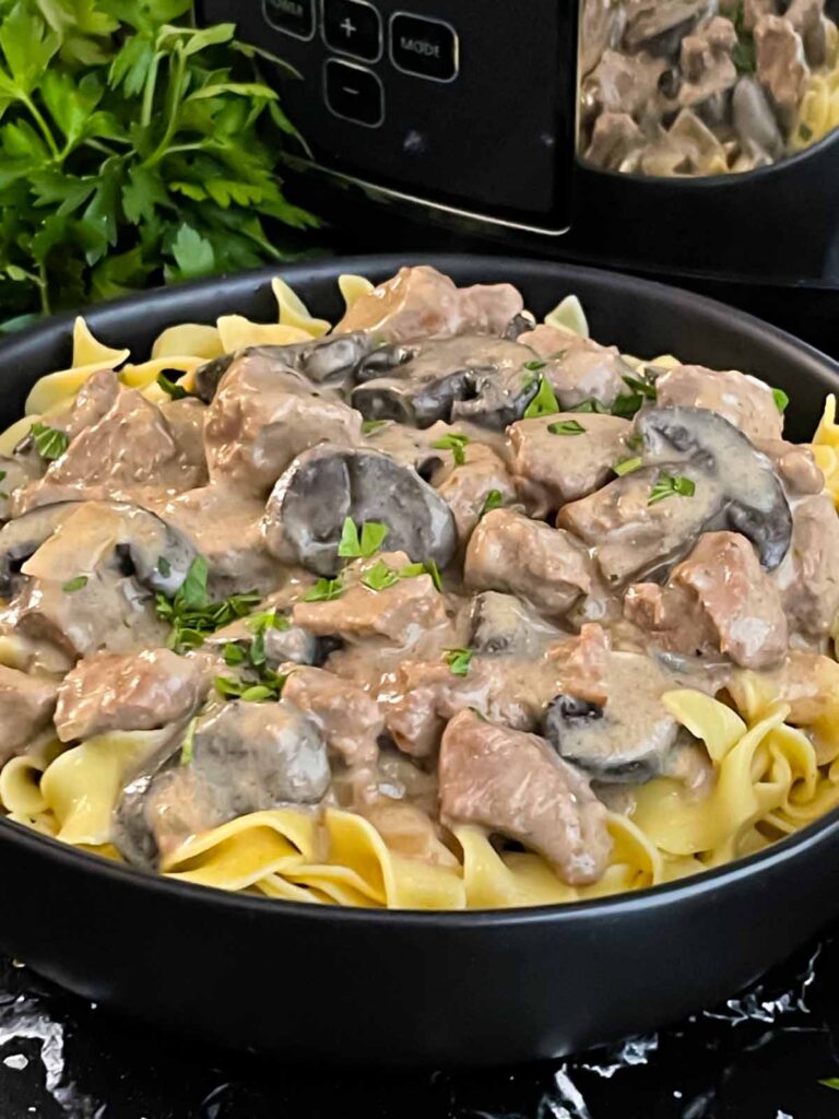 Slow cooker beef stroganoff in a dark bowl, garnished with chopped parsley.