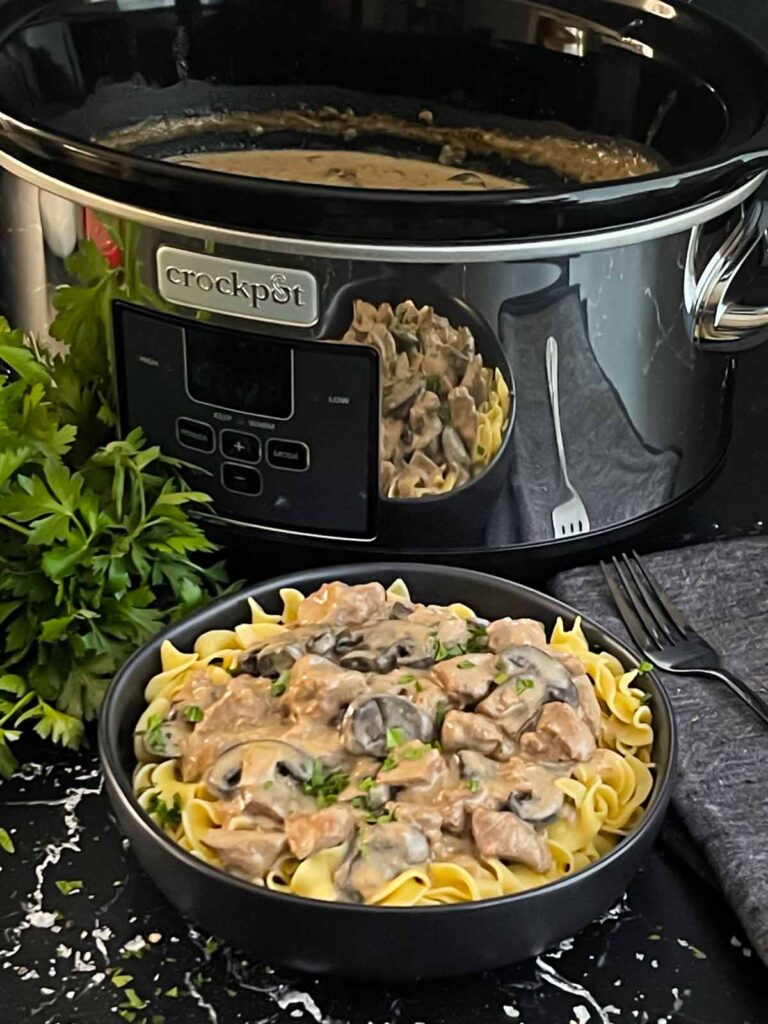 Slow cooker beef stroganoff in a dark bowl, garnished with chopped parsley.