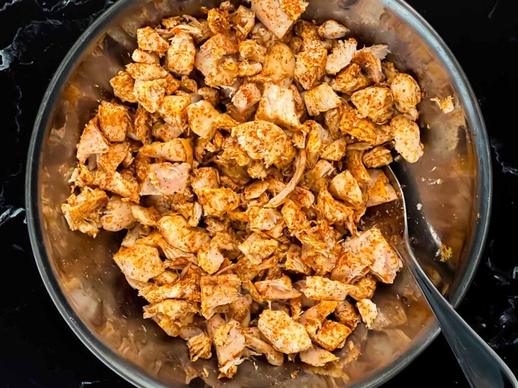 Cooked seasoned chicken in a stainless steel bowl.